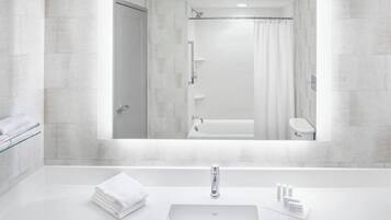 A modern bathroom with a large mirror, a white sink, and a shower.