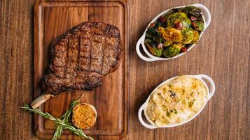 Un bistec sobre una tabla de madera, un plato de brócoli de Bruselas asado y una papa al horno.
