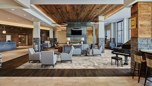 A spacious lobby with a wooden ceiling, a stone fireplace, and a grand piano.