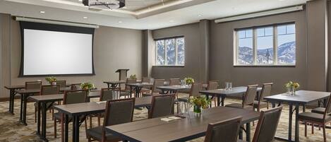 A conference room with multiple tables and chairs, a projector screen, and large windows with a mountain view.
