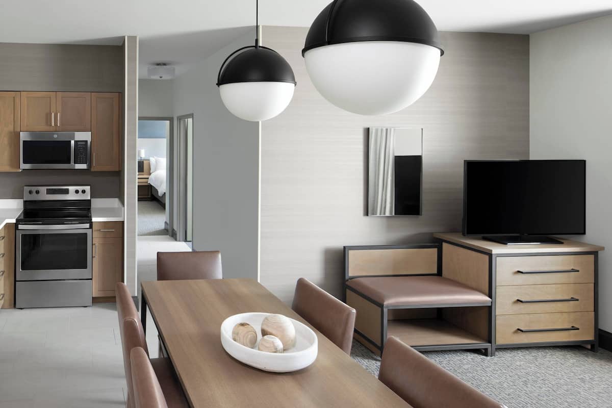 A modern kitchen with stainless steel appliances, a dining area with a wooden table and chairs, and a television on a wooden cabinet.