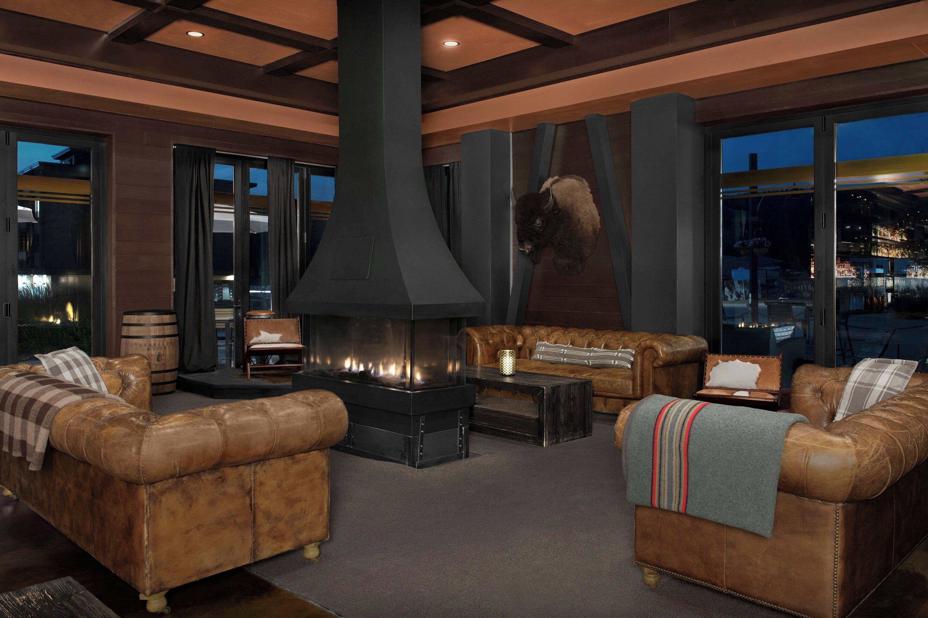 A modern living room with leather sofas, a large fireplace, and large windows offering a city view.