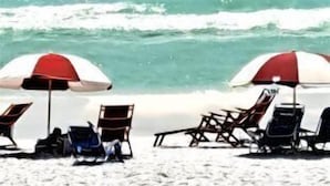 Escena de playa con paracaídas, lancha rápida y sillones de descanso bajo sombrillas.