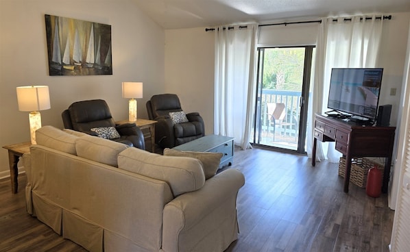 Una sala de estar con un sofá, dos sillones, una mesa de centro, un televisor y un cuadro en la pared.