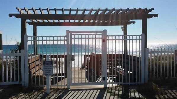 A gated beach entrance with a wooden deck and a pergola.