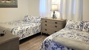Un dormitorio con dos camas, un ventilador de techo, una mesita de noche con lámpara y un aparador.
