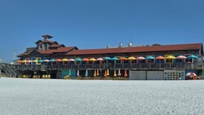 Un edificio frente a la playa con techo rojo y varias sombrillas de colores.