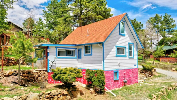 A house with a red roof, white walls, and blue trim. It has a small front porch and a stone foundation. - Vintage Cabin with Hot Tub, Convenient in-Town Location & Mountain Views! #3511 (Estes Park)