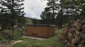 A small wooden cabin with a sloped roof, surrounded by trees and a rocky outcrop. - Vintage Cabin with Hot Tub, Convenient in-Town Location & Mountain Views! #3511 (Estes Park)