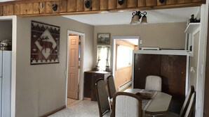 A dining area with a table and chairs, a kitchen area with a refrigerator and cabinets, and a door leading to another room. - Vintage Cabin with Hot Tub, Convenient in-Town Location & Mountain Views! #3511 (Estes Park)