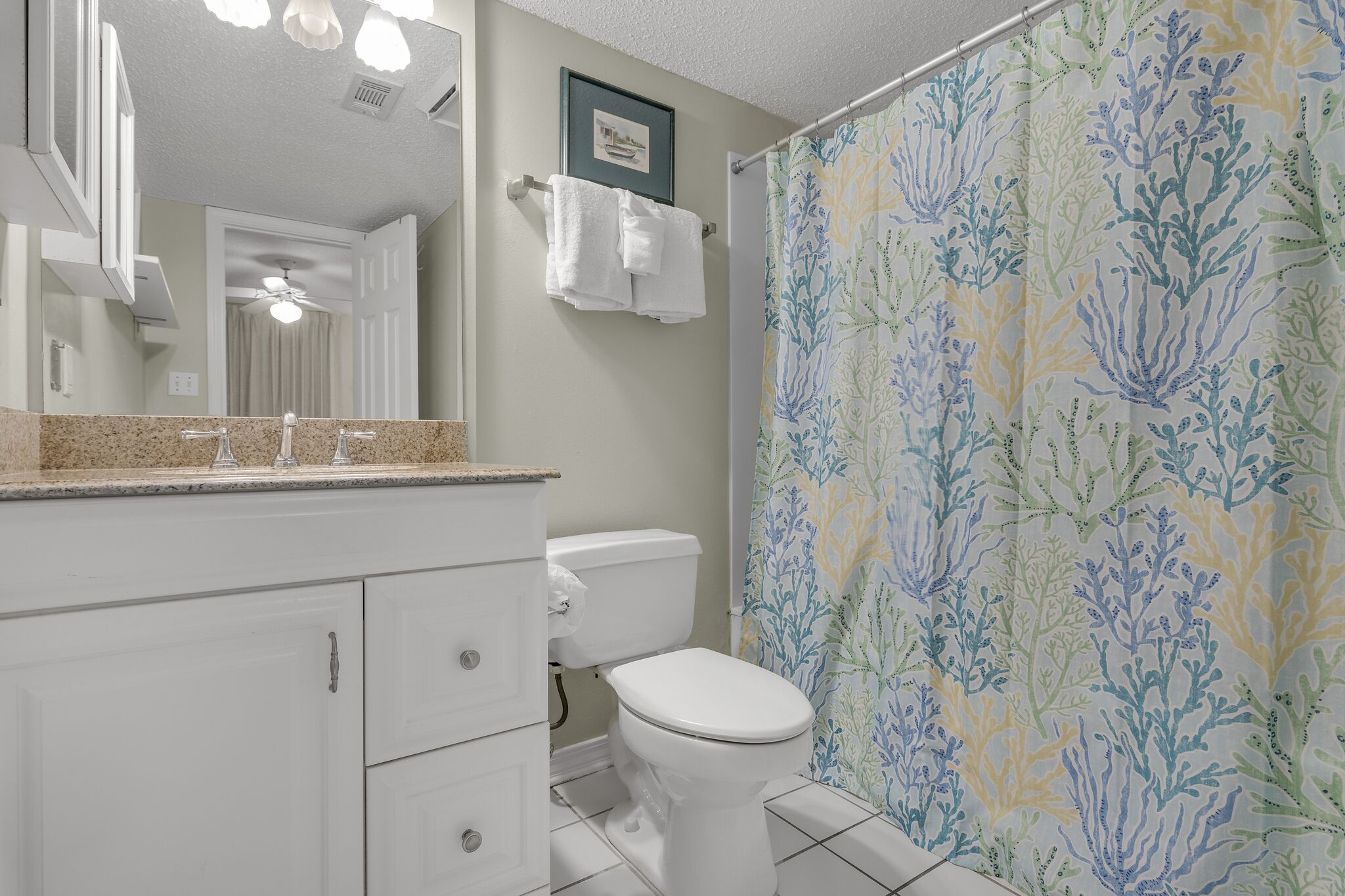 A bathroom with a white toilet, a sink with a mirror above it, and a shower curtain with a blue and green pattern.