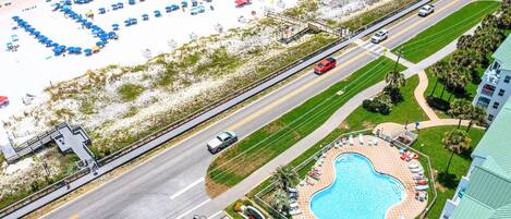 An aerial view of a beach resort with a swimming pool, beach umbrellas, and a road with vehicles.
