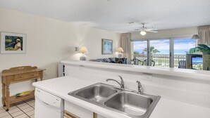 A kitchen with a double sink, a ceiling fan, and a view of the ocean through large windows.