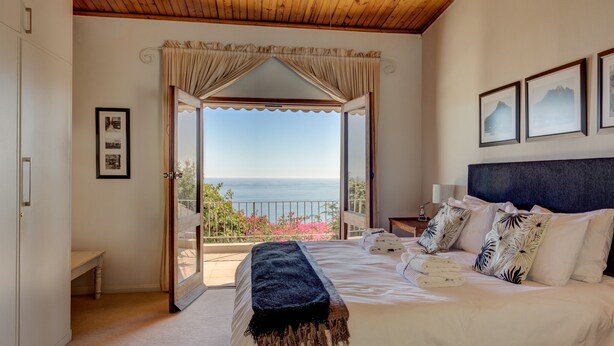 Une chambre avec un grand lit, un plafond en bois, un balcon avec vue sur la mer et des tableaux encadrés accrochés au mur.