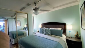 Um quarto com uma cama grande, um ventilador de teto, uma mesa de cabeceira com luminária e um espelho.