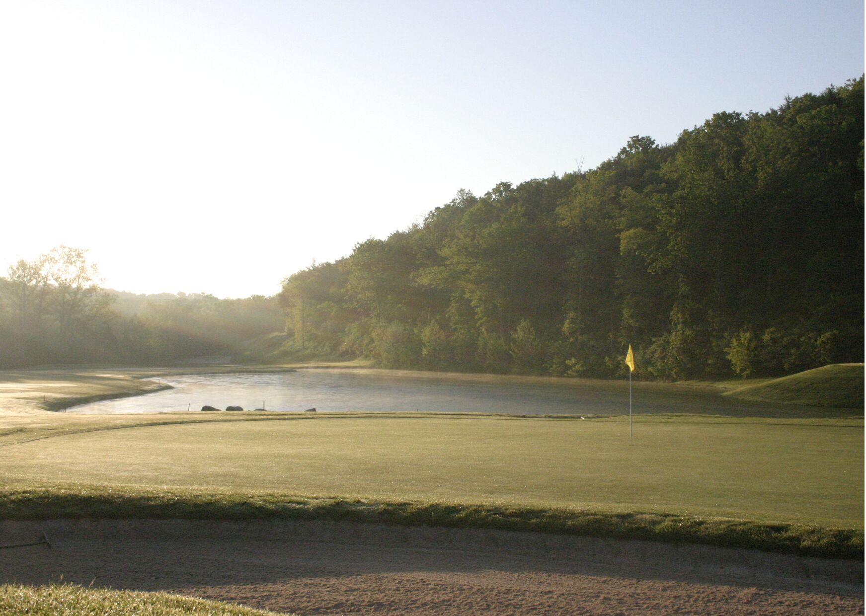 A golf course with a pond, surrounded by trees and a clear sky.