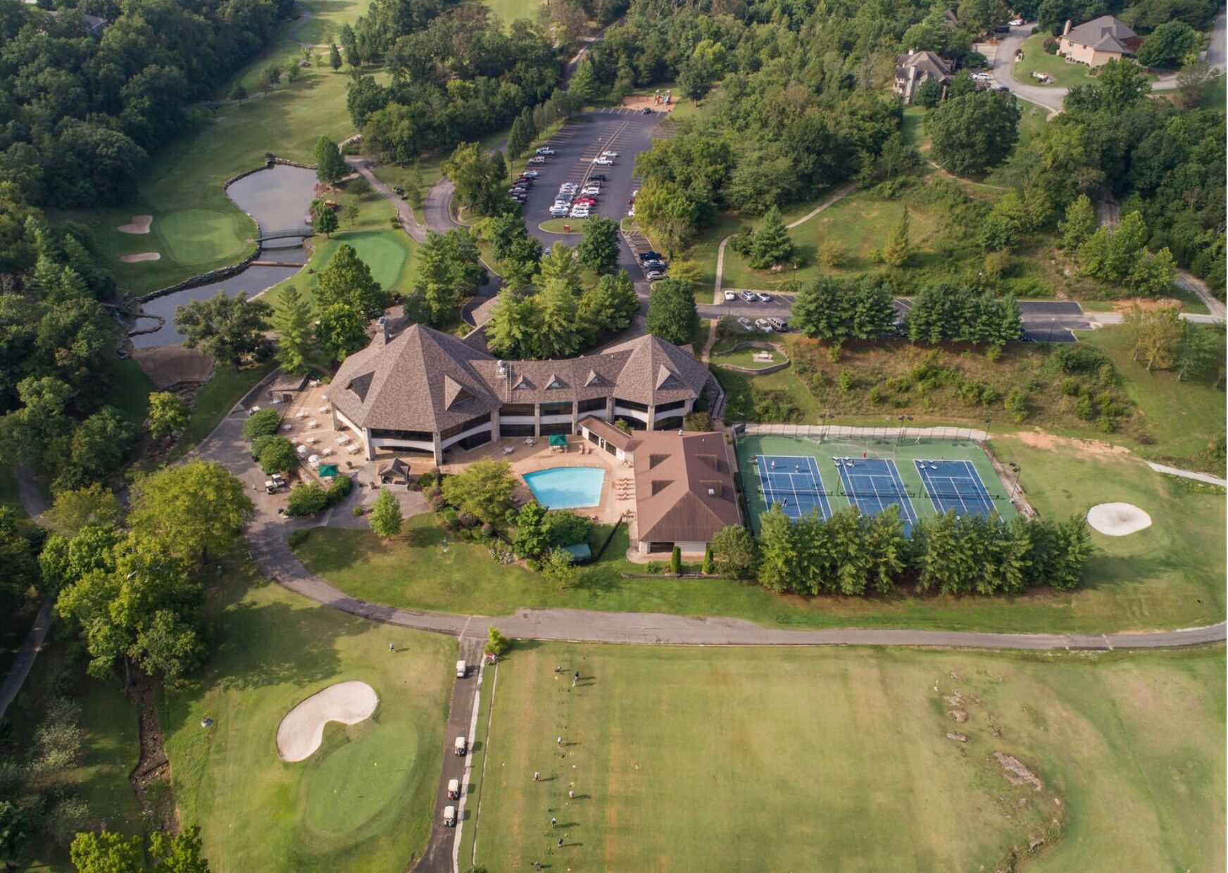 An aerial view of a golf course with a clubhouse, tennis courts, and a swimming pool.
