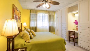 Une chambre d’hôtel équipée d’un lit, d’un bureau, d’une chaise, d’une armoire et d’un ventilateur de plafond.
