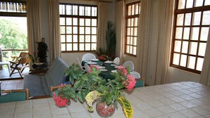A dining area with a table set for four, surrounded by windows with curtains, a sofa, and a chair. - Beautiful pool, 6-min walk from beach, ocean views - VILLAS CASA LOMA - Villa 4 (Playa Flamingo)