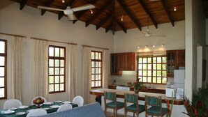 A spacious dining area with a wooden table and chairs, a blue sofa, and a kitchen with wooden cabinets and a window. - Beautiful pool, 6-min walk from beach, ocean views - VILLAS CASA LOMA - Villa 4 (Playa Flamingo)