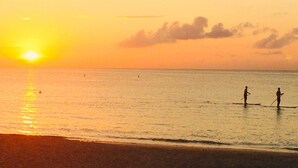 En strandscen vid solnedgången med två personer som åker stående på en bräda.