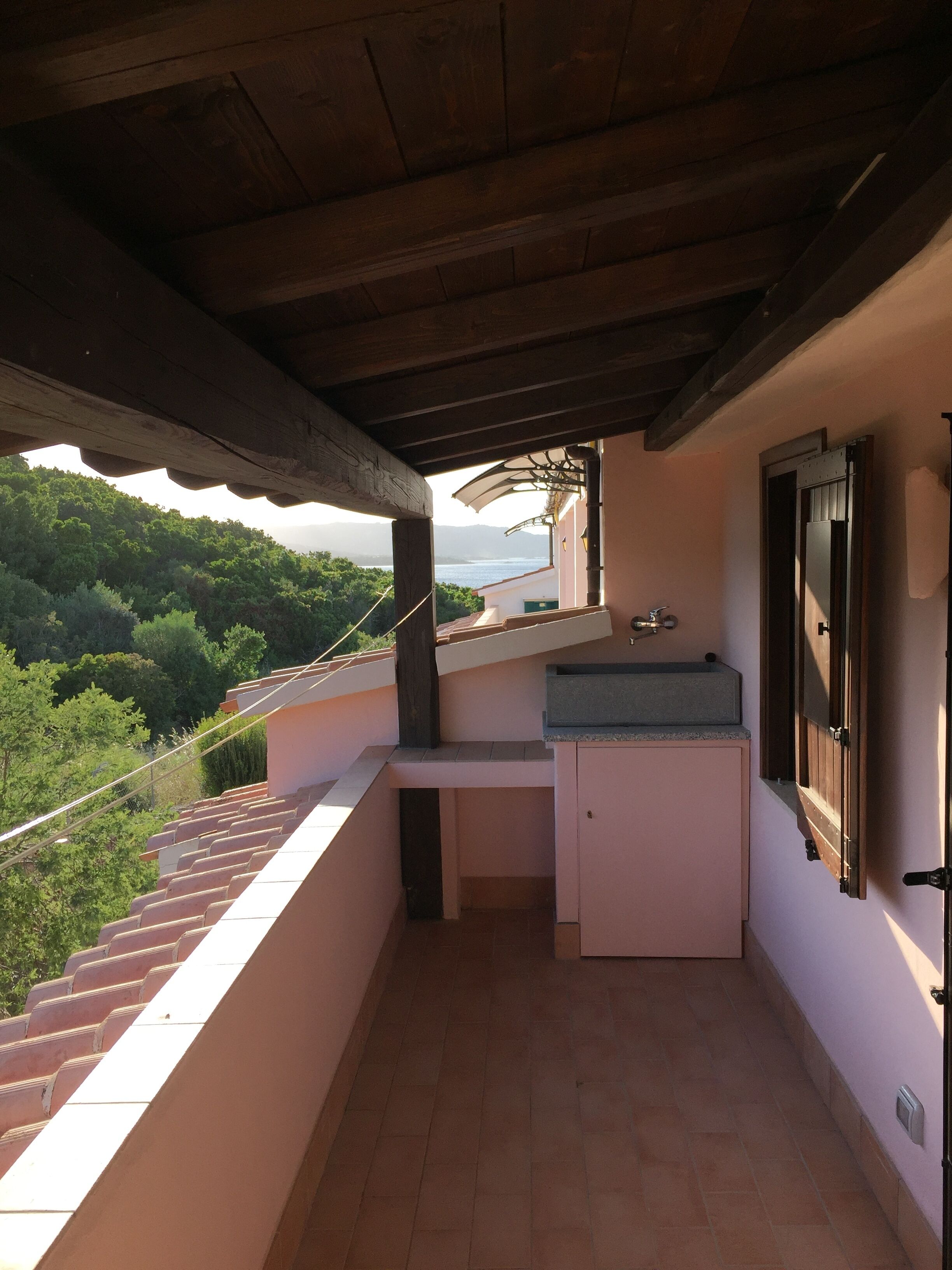 Un balcón con un lavabo y un espejo, con vistas a un paisaje verde exuberante y una masa de agua.