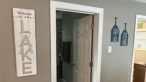 A hallway with a 'Welcome to the LAKE' sign, a door leading to a bathroom, and two 'LAKIN' IT EASY' signs on the wall. - 2-bedroom cabin over looking Kentucky Lake (Benton)