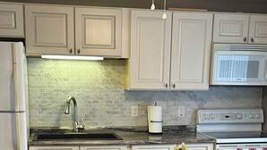 A kitchen with white cabinets, a sink, a stove, and a dining table with placemats. - 2-bedroom cabin over looking Kentucky Lake (Benton)