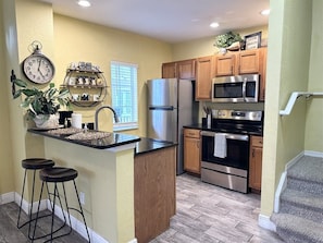 A kitchen with a central island, stainless steel appliances, wooden cabinets, and a clock on the wall. - Venetian Bay 4 Bedroom in Quiet Location - VB014 (Kissimmee)
