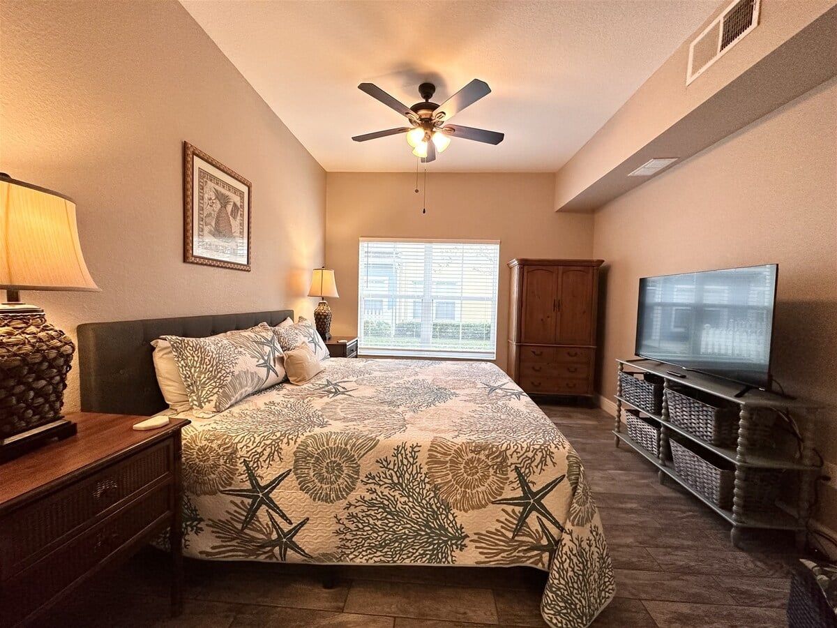 A bedroom with a bed, a ceiling fan, a television, and a window.