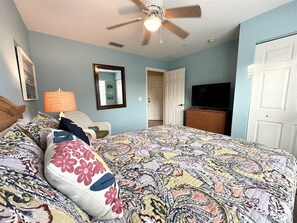 Une chambre à coucher avec un lit, un ventilateur de plafond, un téléviseur et une porte.