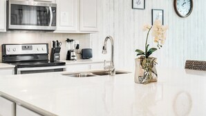 Una cucina con un forno a microonde in acciaio inossidabile, un piano cottura, un lavello e un vaso con fiori.