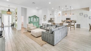 Un'ampia zona giorno con un divano angolare grigio, un mobiletto verde e una cucina sullo sfondo.