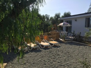 Un'area patio con posti a sedere all'aperto, un piccolo edificio e vegetazione circostante.
