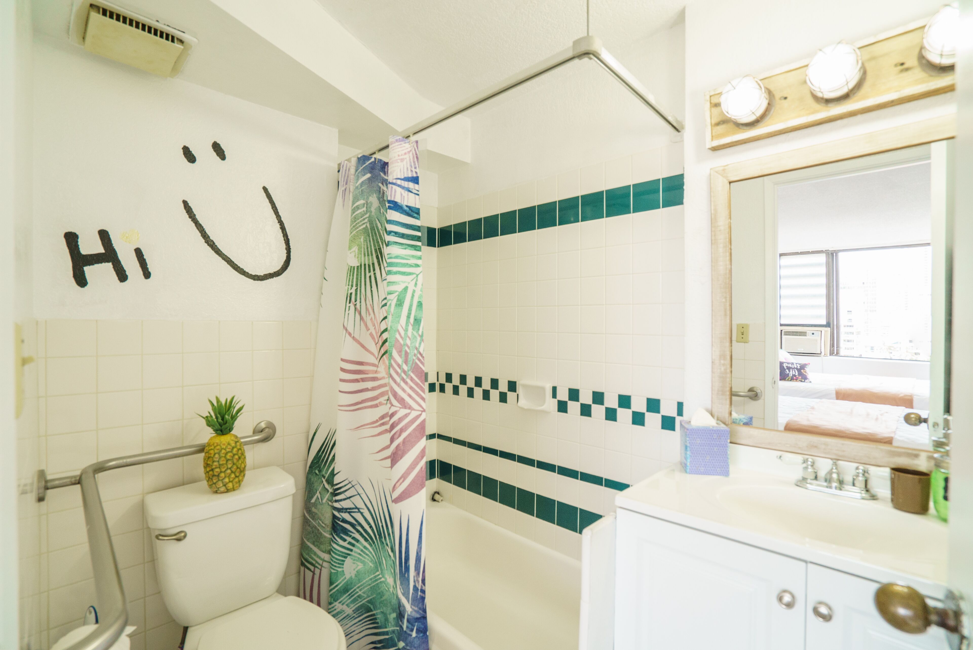 Un bagno con il water, una doccia con tenda a fiori, un lavandino con specchio e un portascopevoli.