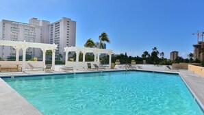 A clear blue pool with lounge chairs and a pergola, surrounded by high-rise buildings and palm trees. - ”Old Hawaii" Great Location at Waikiki (H7) (Honolulu)