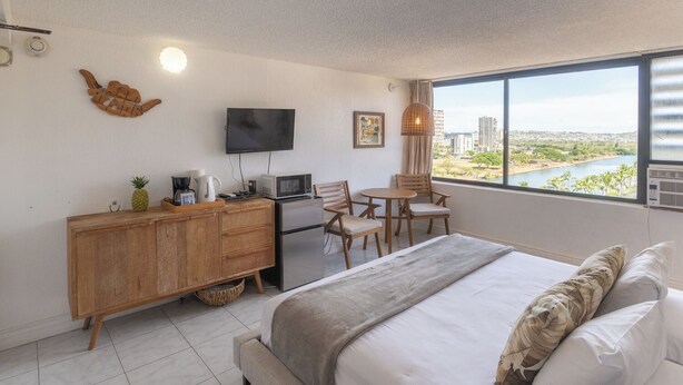 A hotel room with a bed, a desk with a TV, a view of a cityscape, and a window with a view of a river. - ”Old Hawaii" Great Location at Waikiki (H7) (Honolulu)