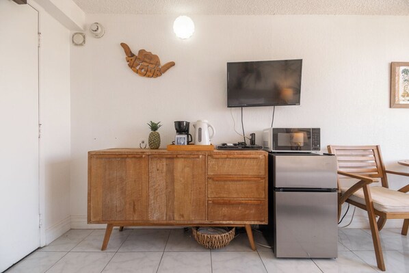 A compact kitchen with a wooden cabinet, a microwave, a coffee maker, and a small table with a chair.