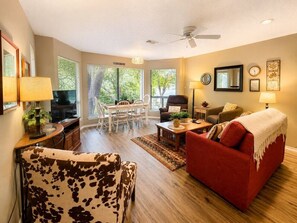 A living room with a red sofa, a cow print armchair, a dining area with a table and chairs, and a ceiling fan.