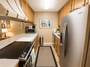 A modern kitchen with stainless steel appliances, wooden cabinets, and a black stovetop.
