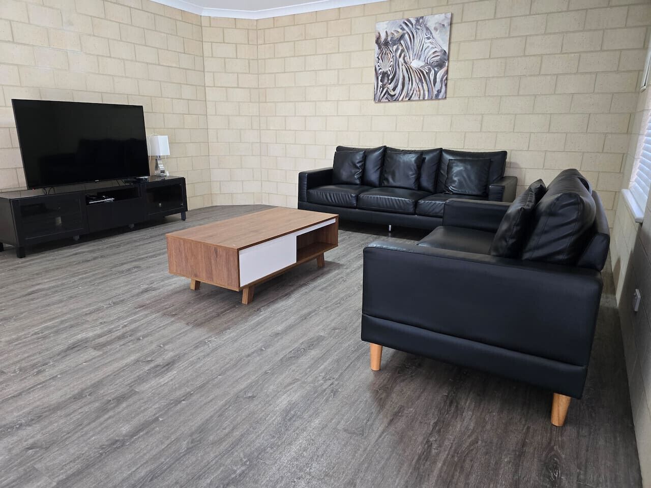 A living room with a TV, a black leather sofa, a wooden coffee table, and a black armchair.