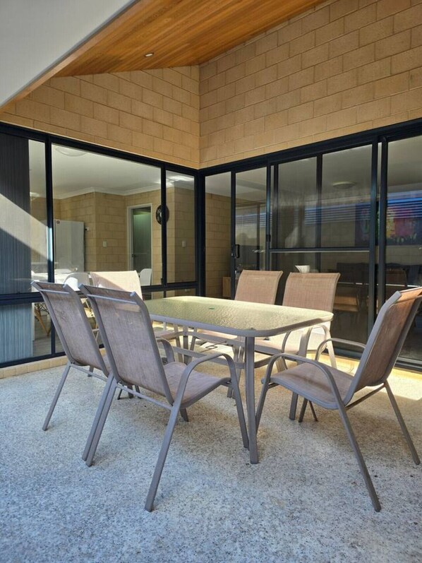 A modern outdoor dining area with a table and chairs, large glass sliding doors, and a brick wall.