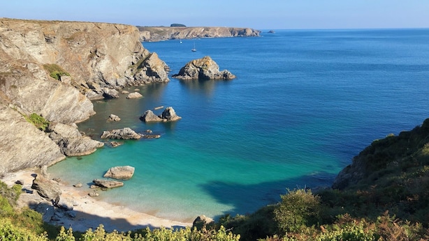 Un paisaje costero con acantilados rocosos, aguas turquesas cristalinas y una pequeña zona de playa.