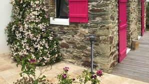 Una casa de piedra con techo inclinado y contraventanas rosadas.
