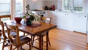 A modern kitchen with white cabinets, a wooden dining table, and a large window. - Luxury Accessible Garden Retreat Near Beaches, Golf & Wineries (Point Lonsdale)