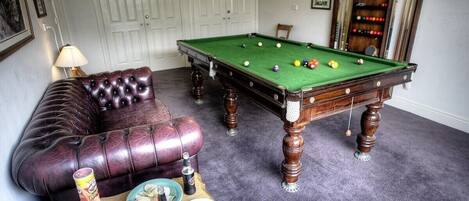 A pool table with balls, a leather sofa, and a small table with drinks and snacks.