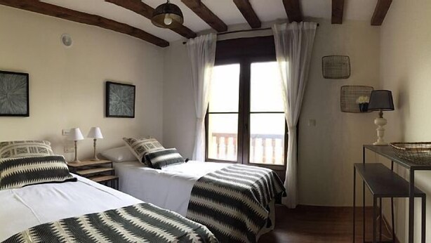 Une chambre avec deux lits, une fenêtre avec des rideaux, une table de chevet avec des lampes et une petite table avec un panier.
