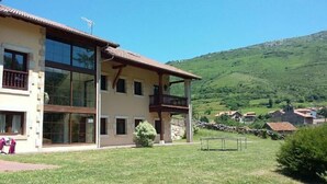 Un bâtiment à deux étages doté de grandes fenêtres, d’un balcon et d’une cour verdoyante.