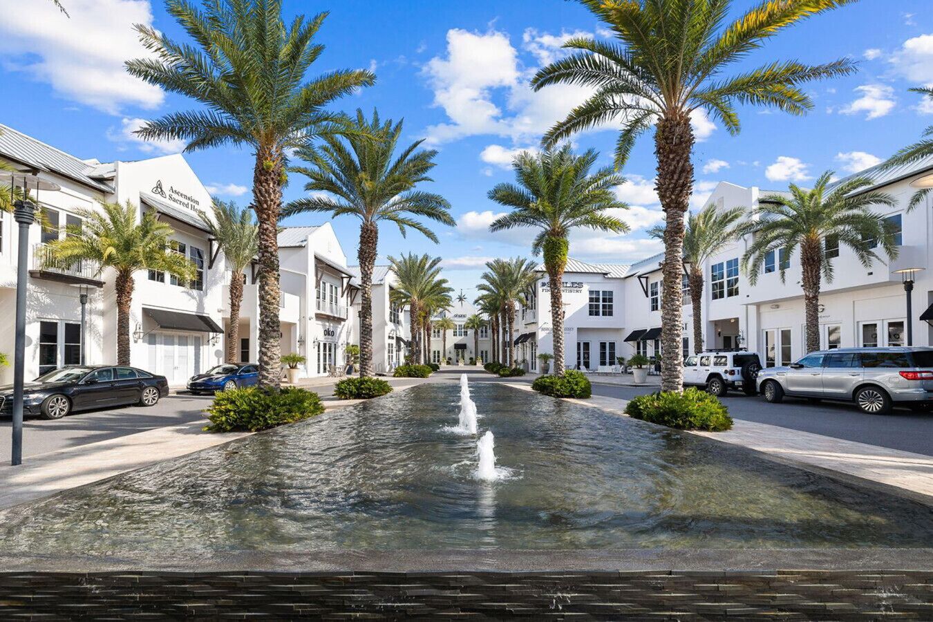 A street lined with palm trees and a fountain in the center.