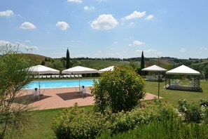 Un espace piscine agrémenté de parasols, de chaises longues et offrant une vue sur des collines verdoyantes.
